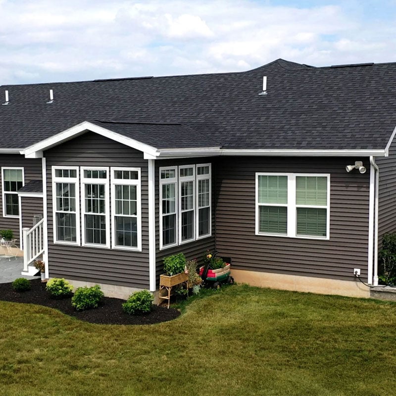 Modern gray house with white trim and black roof A modern gray house with white trim and a black roof, featuring a well-manicured lawn and garden.
