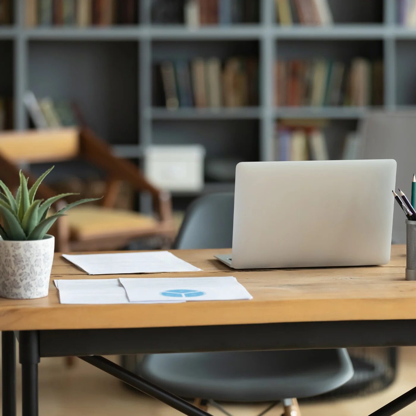Modern office workspace with laptop and papers A laptop on a wooden desk with papers and a plant.