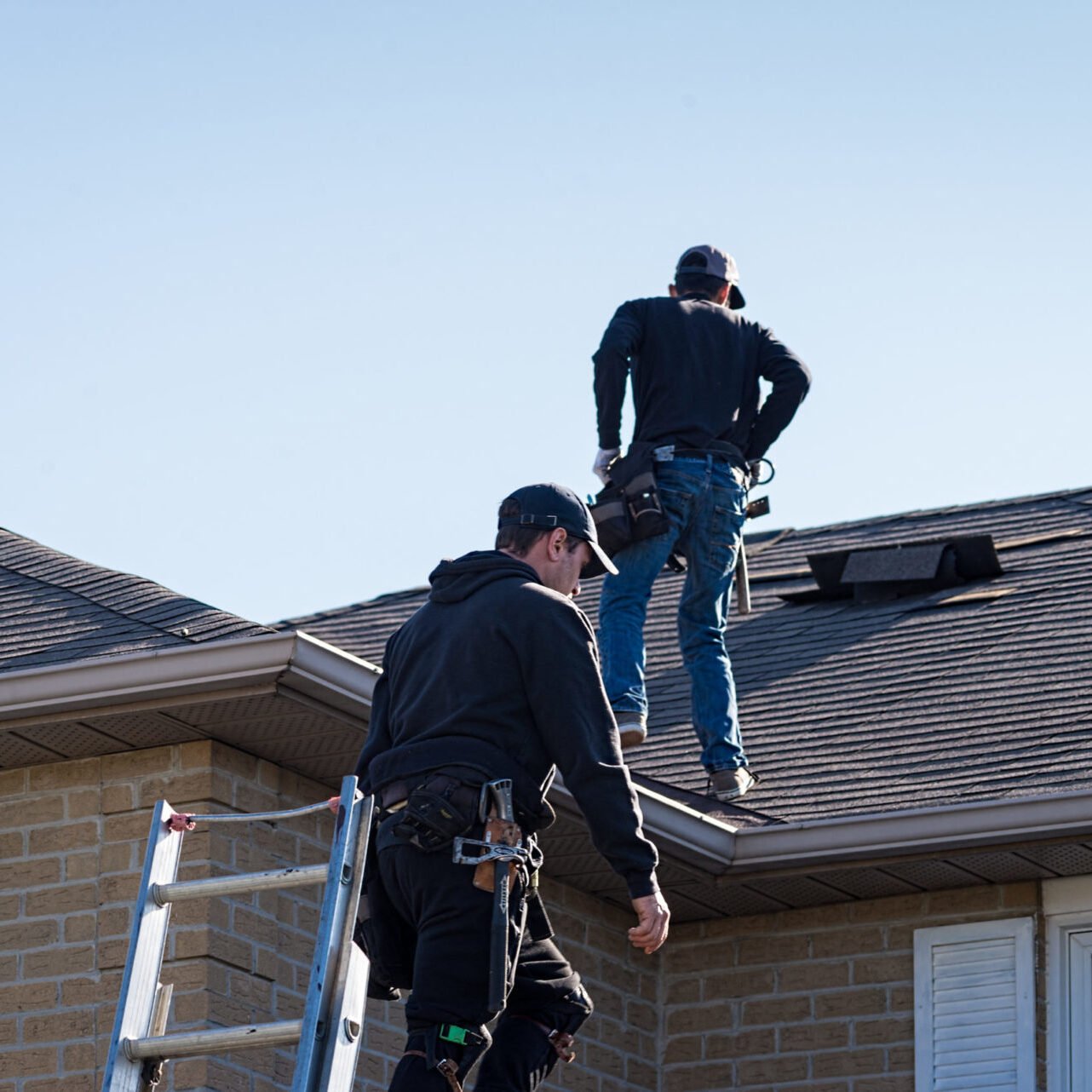 Two men working on a roof Two workers in black clothes on a roof with tools
