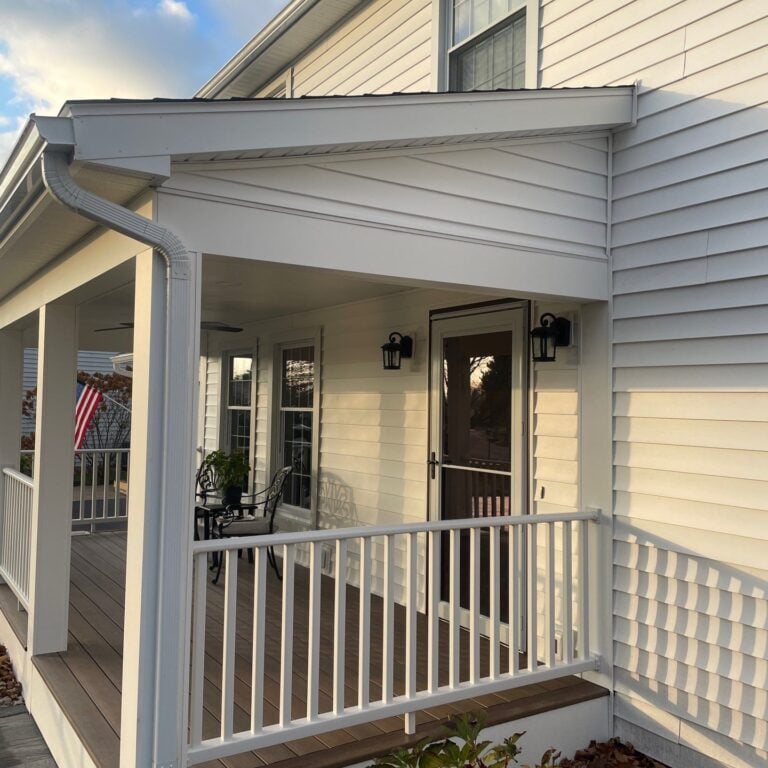 A white house with a covered porch and railing. The porch has a door and windows.